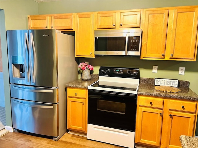 kitchen featuring appliances with stainless steel finishes, dark countertops, and light wood-style flooring