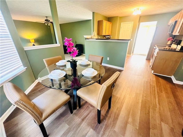 dining space featuring a textured ceiling, light wood-type flooring, a ceiling fan, and baseboards