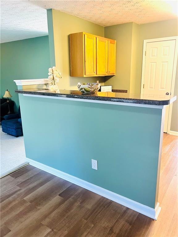 kitchen with a textured ceiling, a peninsula, wood finished floors, baseboards, and dark countertops