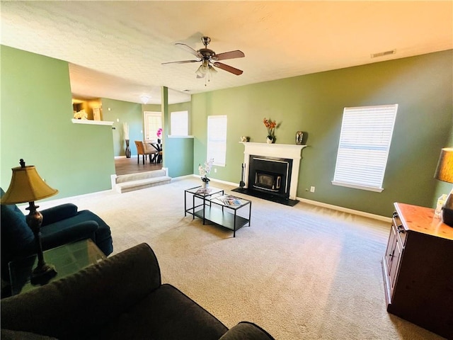 living area with light colored carpet, a fireplace with raised hearth, visible vents, a ceiling fan, and baseboards