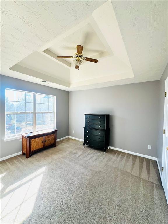 unfurnished bedroom with a textured ceiling, carpet flooring, a raised ceiling, and baseboards