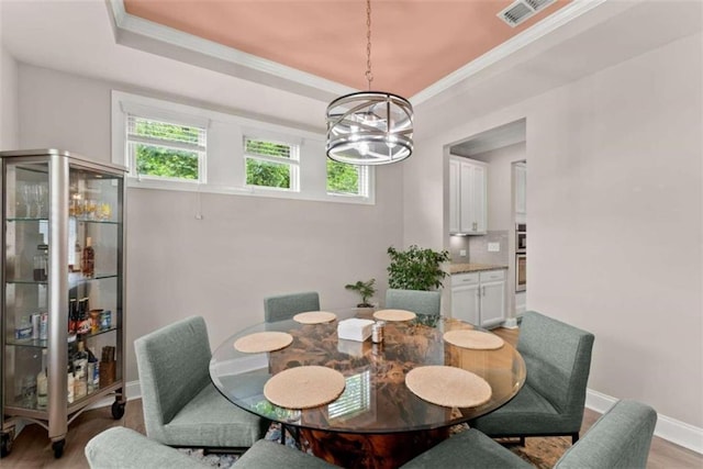 dining room featuring a notable chandelier, a raised ceiling, ornamental molding, and light hardwood / wood-style flooring