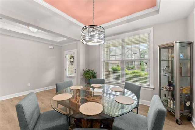 dining space with light hardwood / wood-style floors, a chandelier, a raised ceiling, and ornamental molding