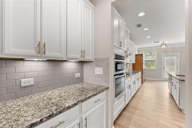 kitchen with light hardwood / wood-style floors, light stone counters, tasteful backsplash, double oven, and white cabinets