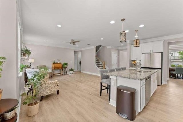 kitchen with white cabinets, a kitchen island with sink, light stone counters, and light hardwood / wood-style flooring