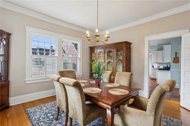 dining area with ornamental molding, a notable chandelier, and light hardwood / wood-style flooring