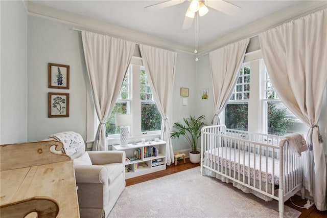 bedroom featuring ceiling fan, hardwood / wood-style floors, and a crib