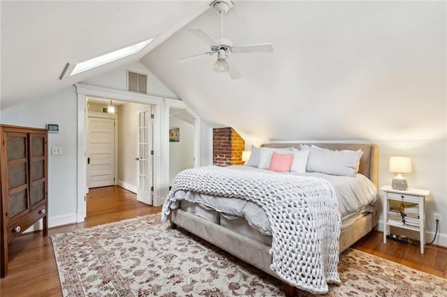 bedroom featuring dark wood-type flooring, vaulted ceiling with skylight, and ceiling fan