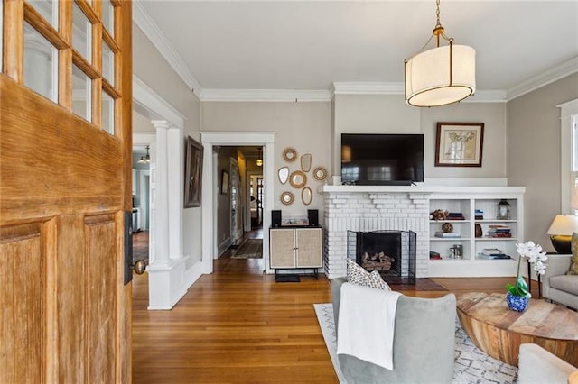 living room featuring ornate columns, crown molding, a brick fireplace, and hardwood / wood-style floors