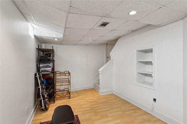 basement with hardwood / wood-style flooring, a paneled ceiling, and built in shelves