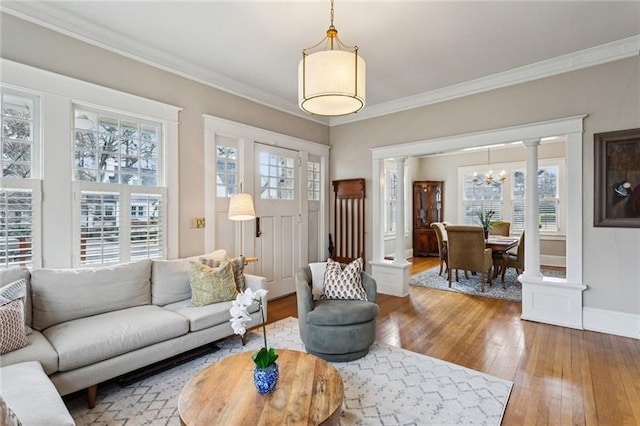 living room featuring an inviting chandelier, hardwood / wood-style floors, ornamental molding, and ornate columns