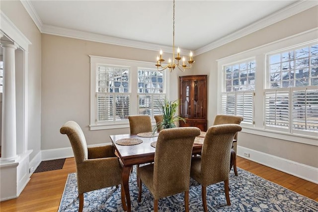 dining space featuring ornate columns, ornamental molding, a chandelier, and light hardwood / wood-style floors