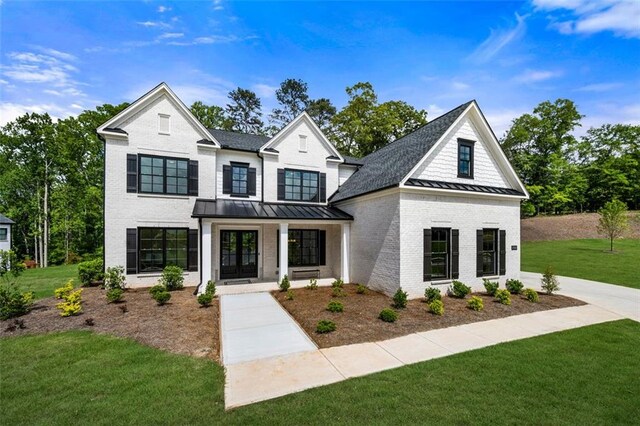 view of front of home with a standing seam roof, a front lawn, french doors, brick siding, and a shingled roof