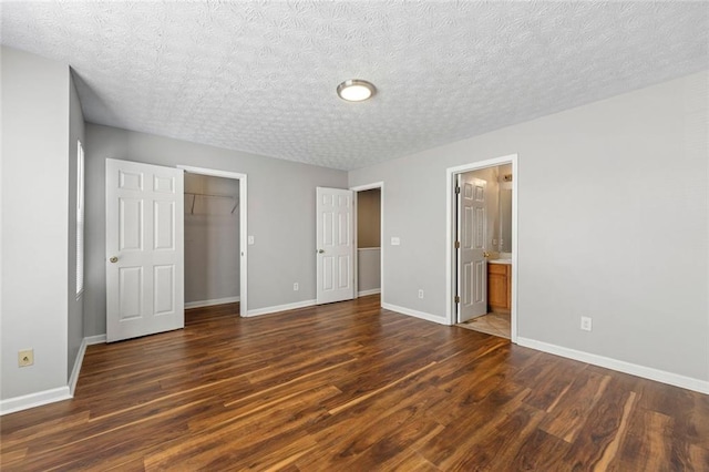 unfurnished bedroom with a walk in closet, baseboards, dark wood finished floors, and a closet