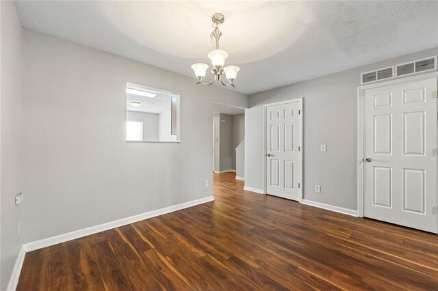 spare room with baseboards, dark wood-type flooring, visible vents, and an inviting chandelier