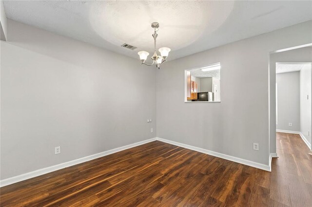 empty room featuring dark wood-style flooring, visible vents, baseboards, and an inviting chandelier