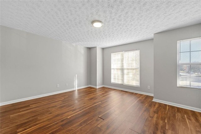 spare room featuring plenty of natural light, baseboards, dark wood finished floors, and a textured ceiling