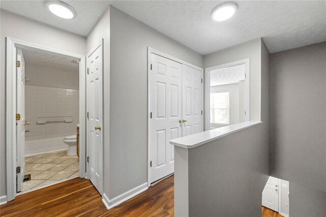 hall featuring a textured ceiling, dark wood finished floors, an upstairs landing, and baseboards