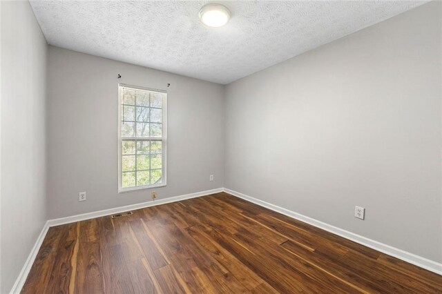 unfurnished room featuring baseboards, visible vents, dark wood finished floors, and a textured ceiling