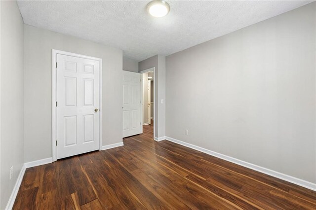 unfurnished bedroom featuring dark wood-style flooring, a textured ceiling, and baseboards