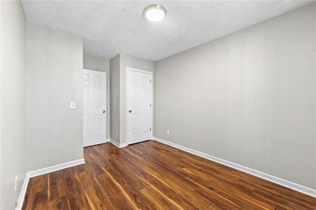 unfurnished bedroom with dark wood-style flooring, a textured ceiling, and baseboards