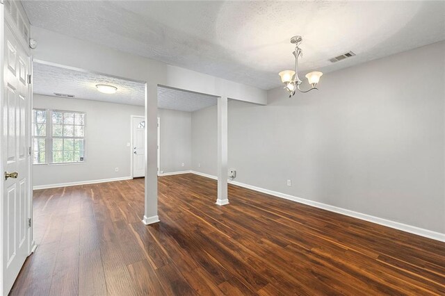 below grade area featuring baseboards, visible vents, dark wood-type flooring, a textured ceiling, and a chandelier