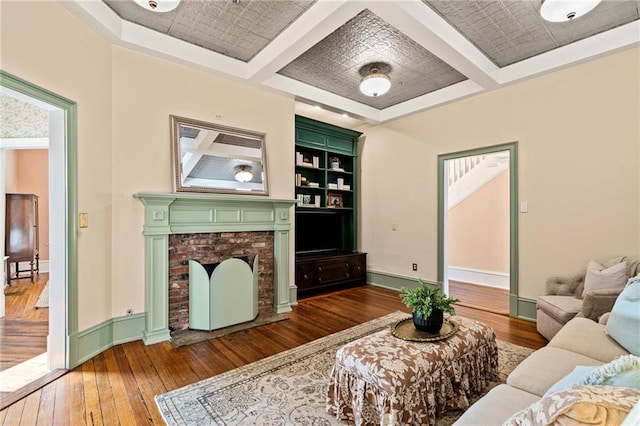 living room featuring hardwood / wood-style floors, coffered ceiling, a fireplace, built in shelves, and beamed ceiling