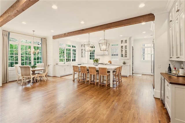dining area with recessed lighting, beamed ceiling, a wealth of natural light, and light wood-style flooring
