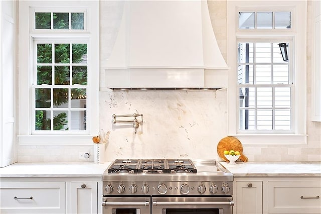 kitchen with decorative backsplash, white cabinetry, double oven range, and light stone countertops