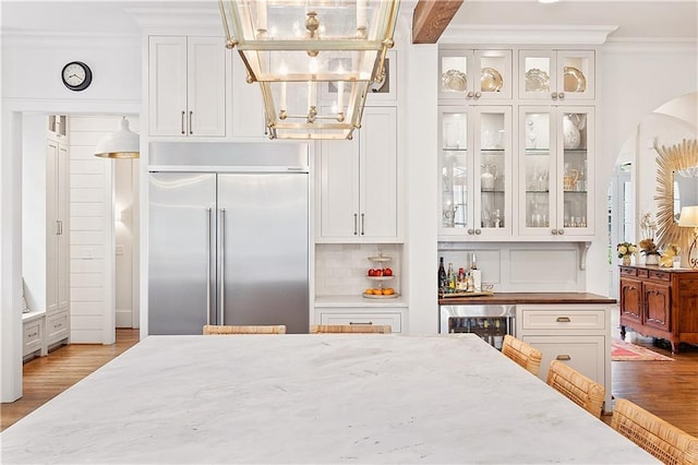 kitchen featuring stainless steel built in fridge, wood finished floors, light stone counters, white cabinets, and ornamental molding