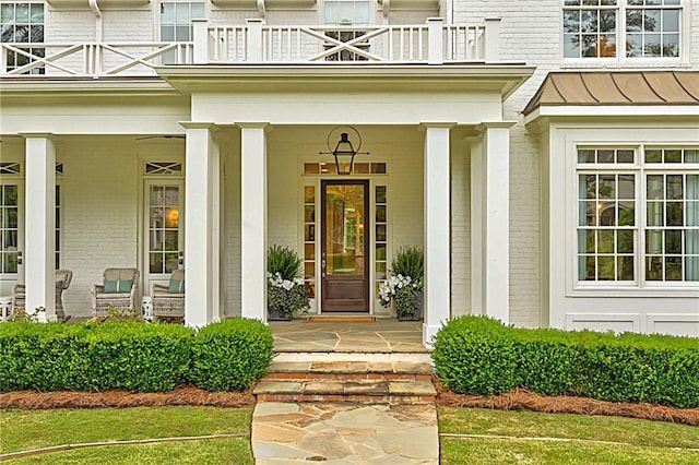 property entrance with brick siding, a balcony, a standing seam roof, and a porch