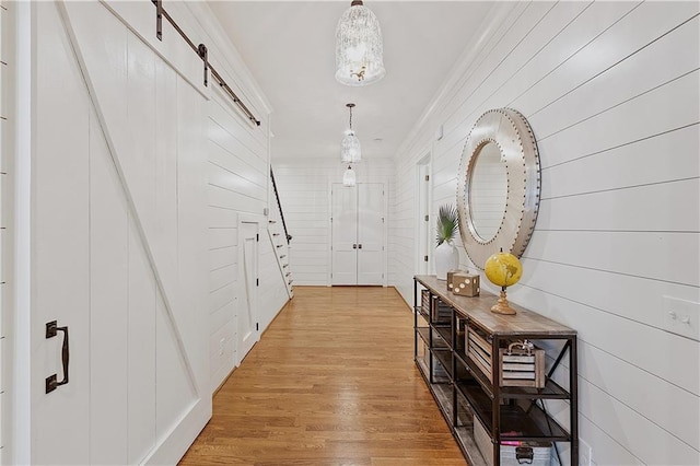 hallway with a barn door, ornamental molding, and light wood-type flooring