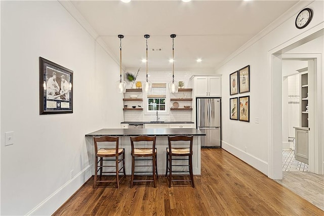 kitchen featuring open shelves, a sink, a breakfast bar area, freestanding refrigerator, and a peninsula
