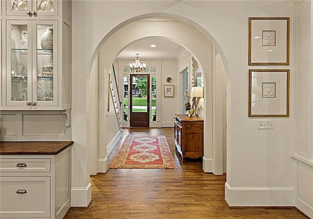 interior space with baseboards, arched walkways, dark wood-style flooring, and a notable chandelier