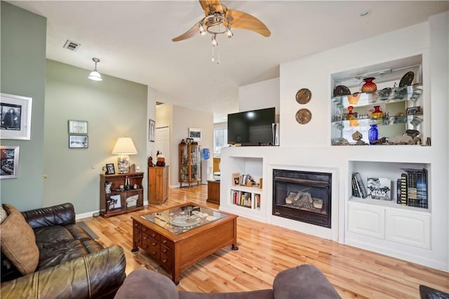 living room featuring hardwood / wood-style floors, built in shelves, and ceiling fan