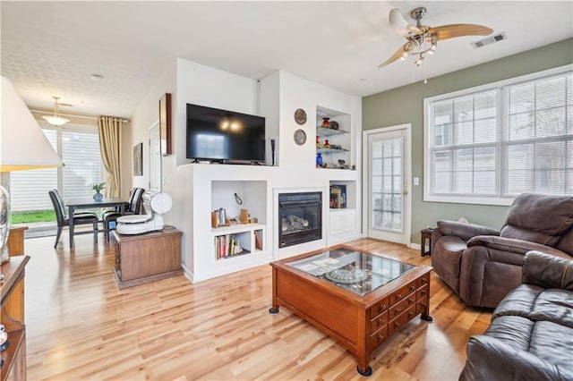 living room with built in features, light hardwood / wood-style floors, and ceiling fan