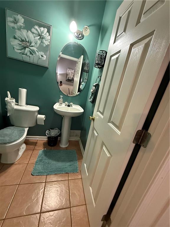 half bathroom featuring a sink, baseboards, toilet, and tile patterned flooring