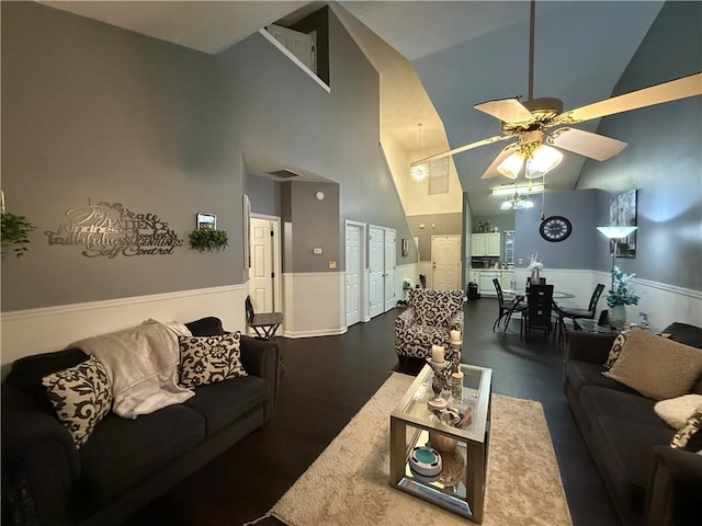 living area with visible vents, a high ceiling, a ceiling fan, and a wainscoted wall
