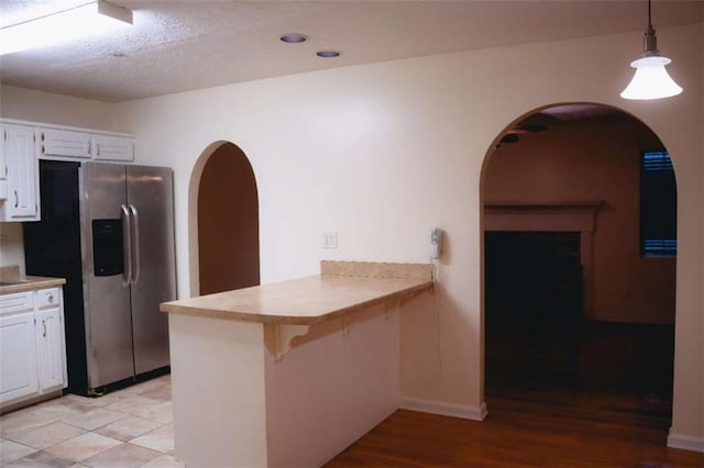 kitchen with stainless steel refrigerator with ice dispenser, pendant lighting, white cabinets, and kitchen peninsula