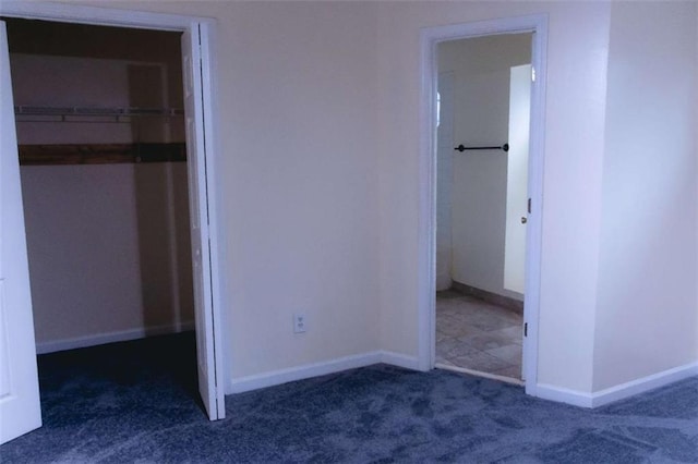 unfurnished bedroom featuring dark carpet, a walk in closet, and a closet