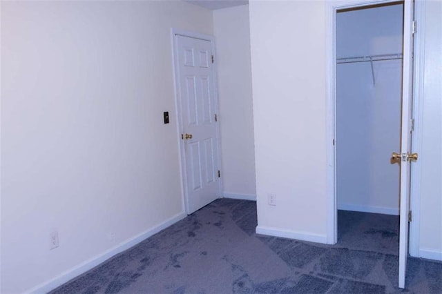 unfurnished bedroom featuring a walk in closet, dark carpet, and a closet