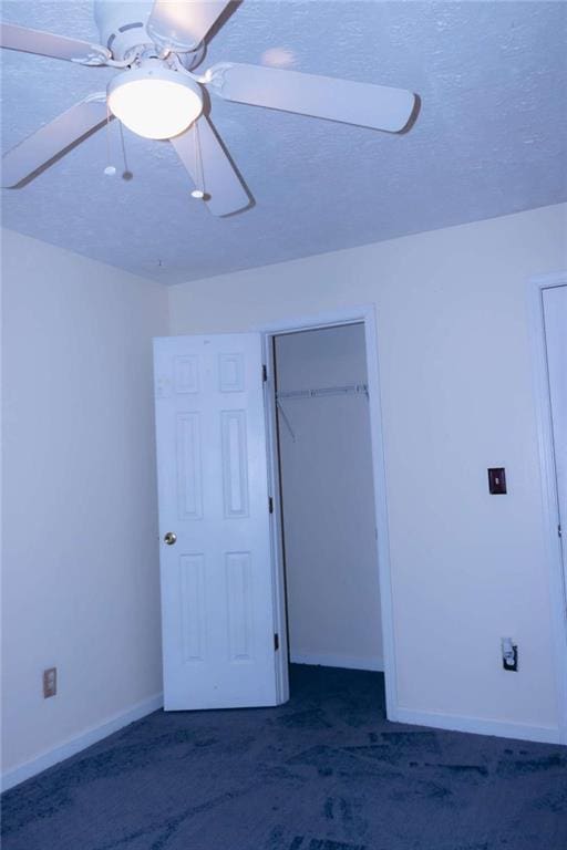 unfurnished bedroom with dark colored carpet, ceiling fan, and a textured ceiling