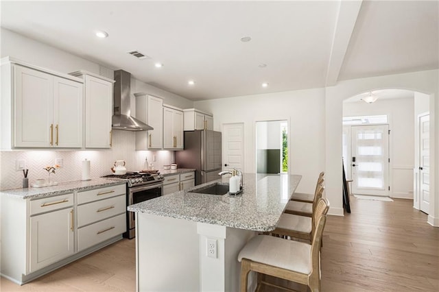 7985 Welch Ml, Ball Ground, GA 30107 - kitchen featuring wall chimney range hood, appliances with stainless steel finishes, a sink, arched walkways, and a center island with sink