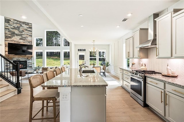 7985 Welch Ml, Ball Ground, GA 30107 - kitchen with stainless steel gas range, wall chimney range hood, a breakfast bar area, light stone countertops, and light wood-style flooring