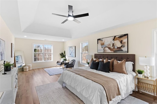 bedroom with light wood-type flooring, multiple windows, a tray ceiling, and recessed lighting