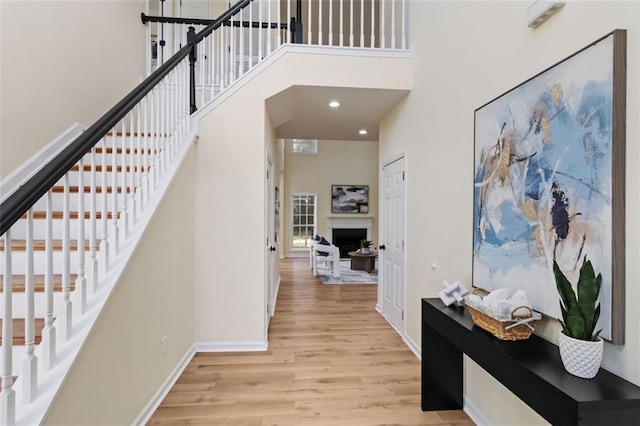 hall with recessed lighting, a high ceiling, baseboards, light wood-style floors, and stairway