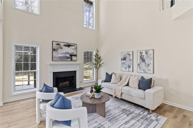 living area with a fireplace, wood finished floors, a towering ceiling, and baseboards