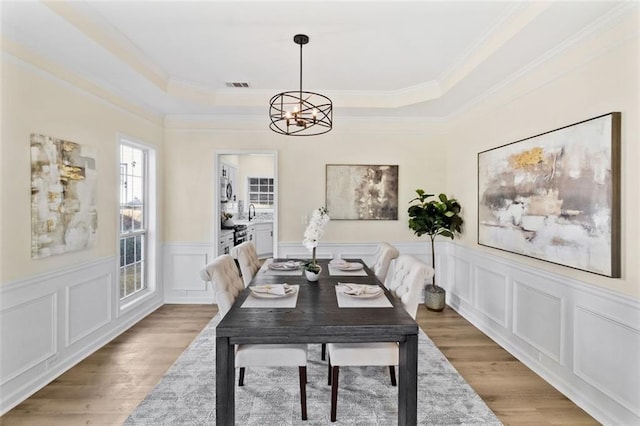 dining space featuring a tray ceiling, visible vents, a notable chandelier, and wood finished floors