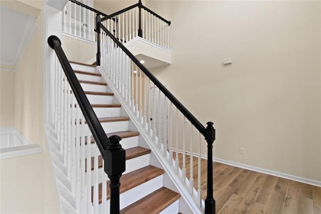 stairs featuring crown molding, a high ceiling, wood finished floors, and baseboards