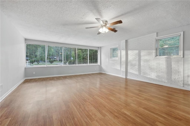 empty room with ceiling fan, hardwood / wood-style floors, a textured ceiling, and a wealth of natural light